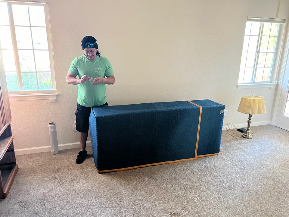 Green-shirted Murdock's Moving & Storage mover drapes a moving blanket over an armchair in a living room