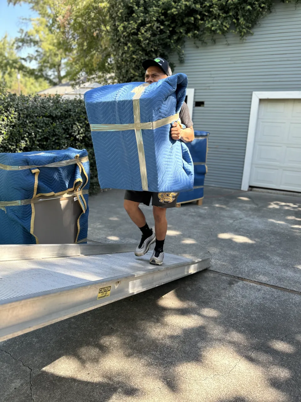 Murdock's Moving & Storage mover guides a hand truck of blanket-wrapped furniture down a ramp from the moving truck