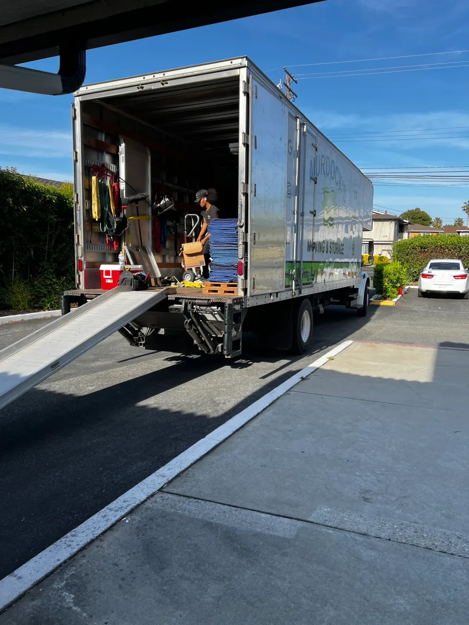 Murdock's Moving crew member loading stacked moving blankets and a dolly on the truck liftgate