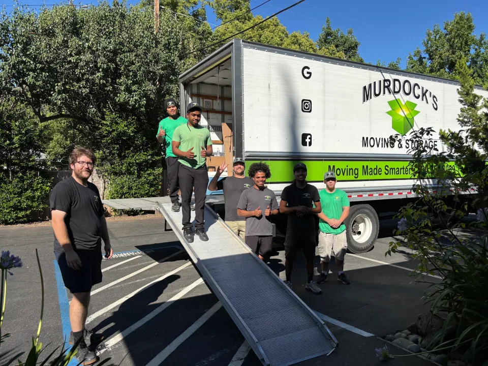 Three Murdock's Moving crew members on the loading ramp of an open box truck in a residential driveway