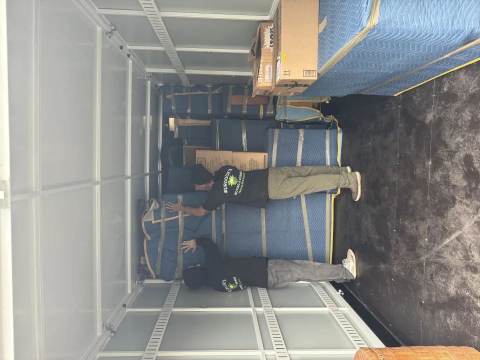 Two Murdock's Moving & Storage movers carefully stack blanket-wrapped furniture inside a loaded moving truck