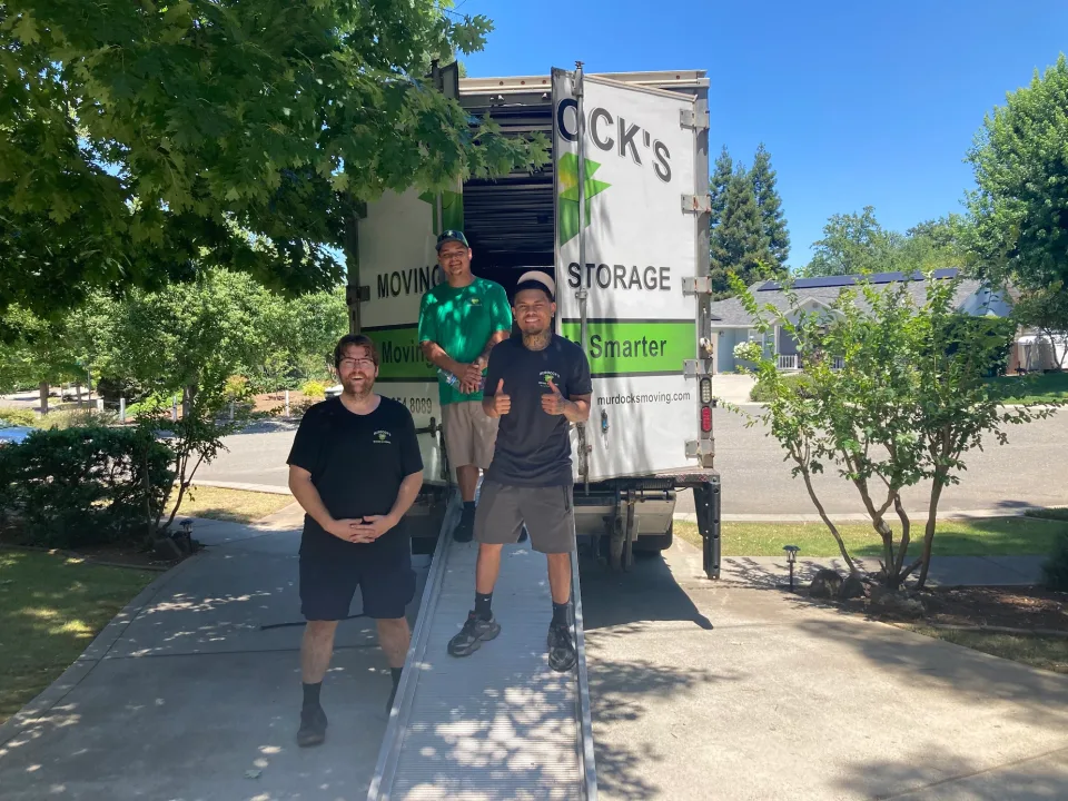 Group of Murdock's Moving & Storage crew members posing at the truck's loading ramp giving thumbs up