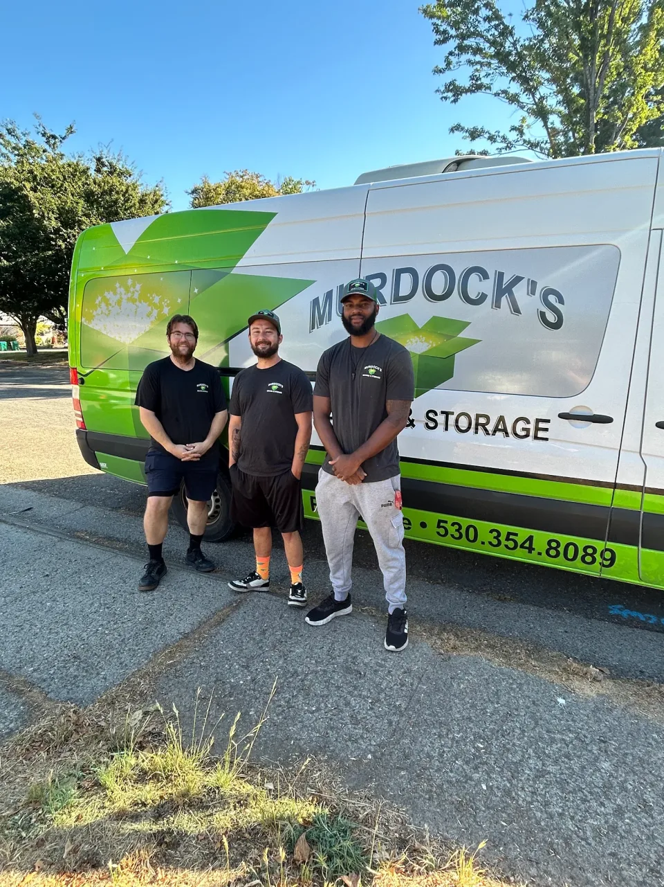Three Murdock's Moving & Storage crew members in green shirts give thumbs up beside the branded box truck