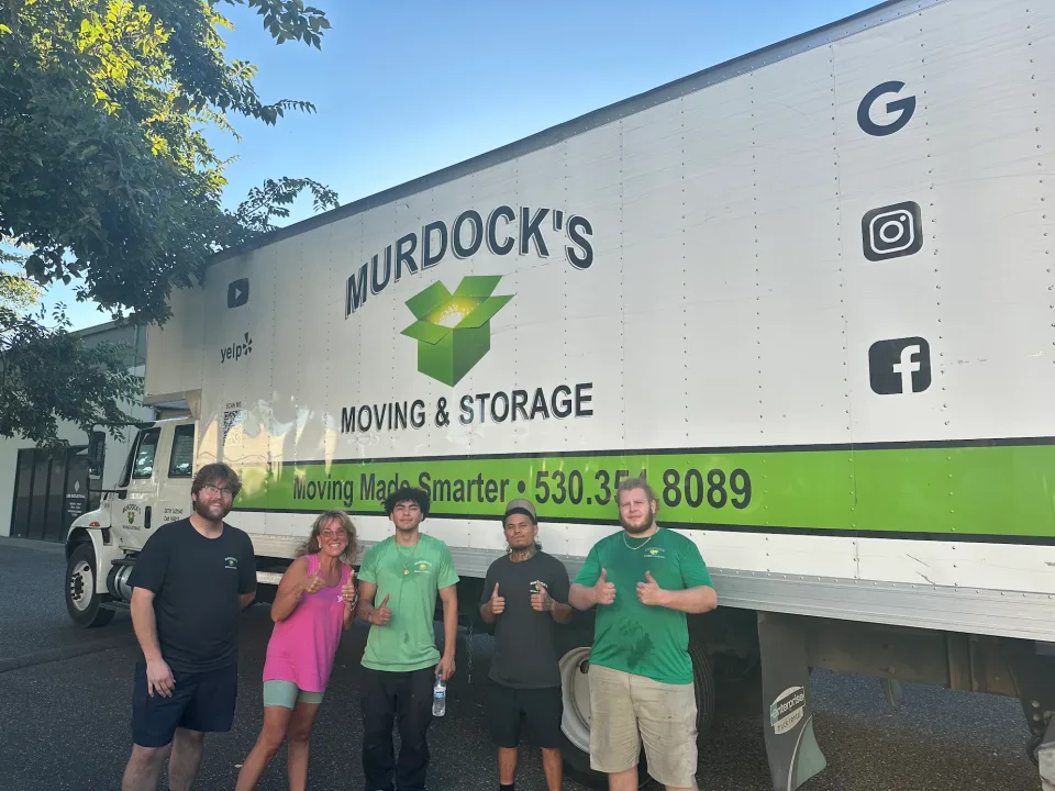 Four Murdock's Moving & Storage movers and a smiling female customer give thumbs up beside the branded truck
